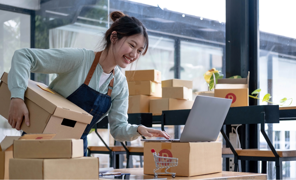 A-woman-using-a-laptop-while-holding-a-box